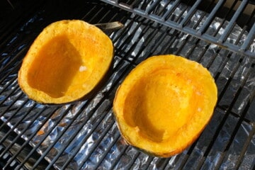 acorn squash smoking on the grates of a pellet grill