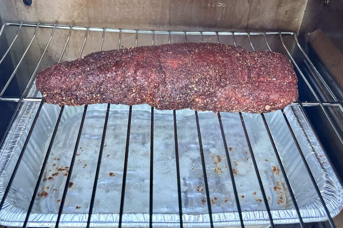 a raw pork tenderloin on the grates inside a masterbuilt electric smoker