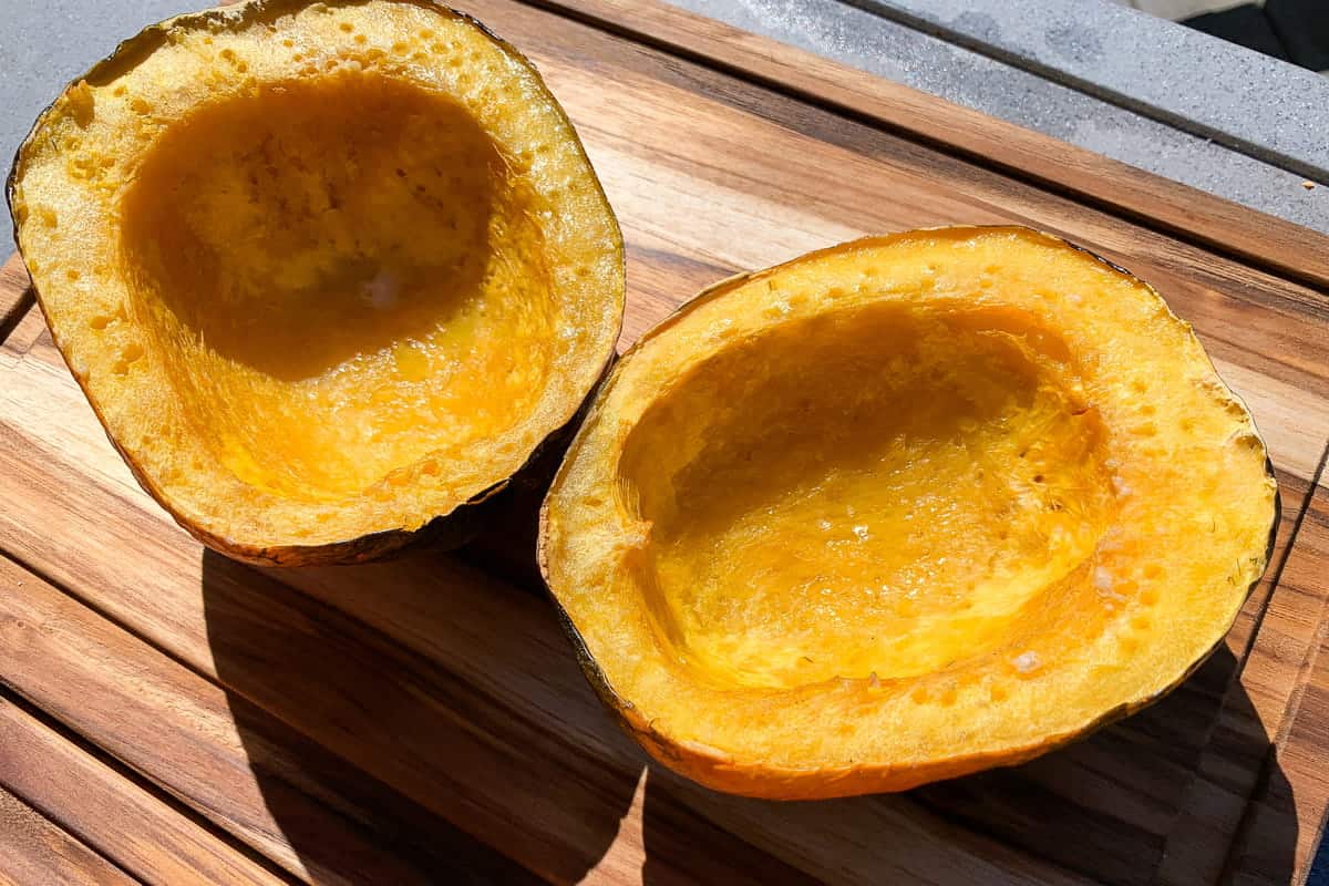 two halves of a smoked acorn squash on a cutting board