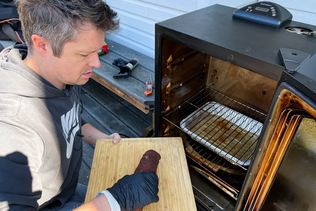 Mads removing the pork tenderloin from the Masterbuilt electric smoker to a wooden cutting board