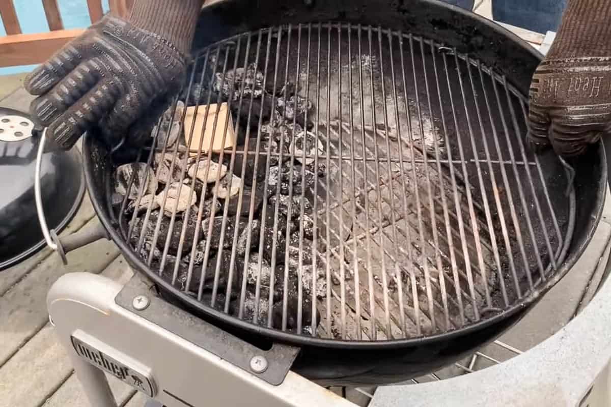 the grate of a charcoal grill placed on top of a a pile of lit charcoal briquettes with a piece of wood on top