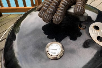 a gloved hand placing the lid on top of a weber charcoal grill