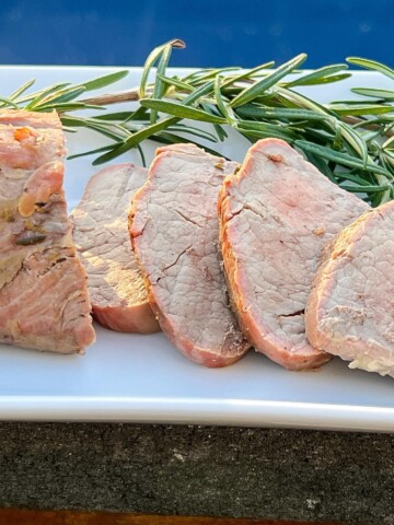 Smoked Pork Tenderloin sliced on a white plate with fresh rosemary on the side as garnish