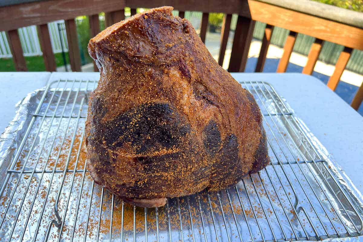 a cold ham seasoned with BBQ rub on a wire rack over an aluminum foil lined baking sheet