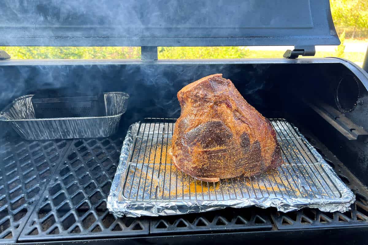 a half ham cut side down on a wire rack over a baking sheet on the grates of a Pit Boss pellet grill