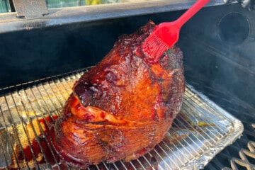 a red silicone spatula brushing cherry glaze onto the surface of a ham on a wire rack