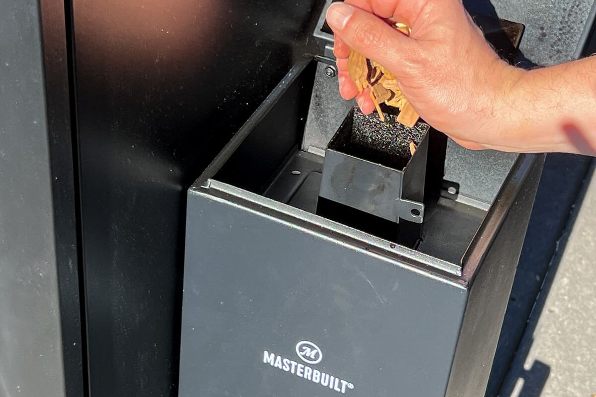 a hand dropping wood chips into the Masterbuilt cold smoker attachment