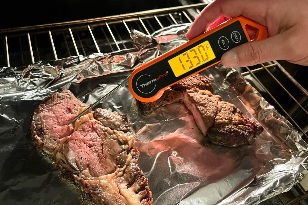 slices of prime rib on a foil covered baking sheet with an instant read thermometer measuring 133 degrees F