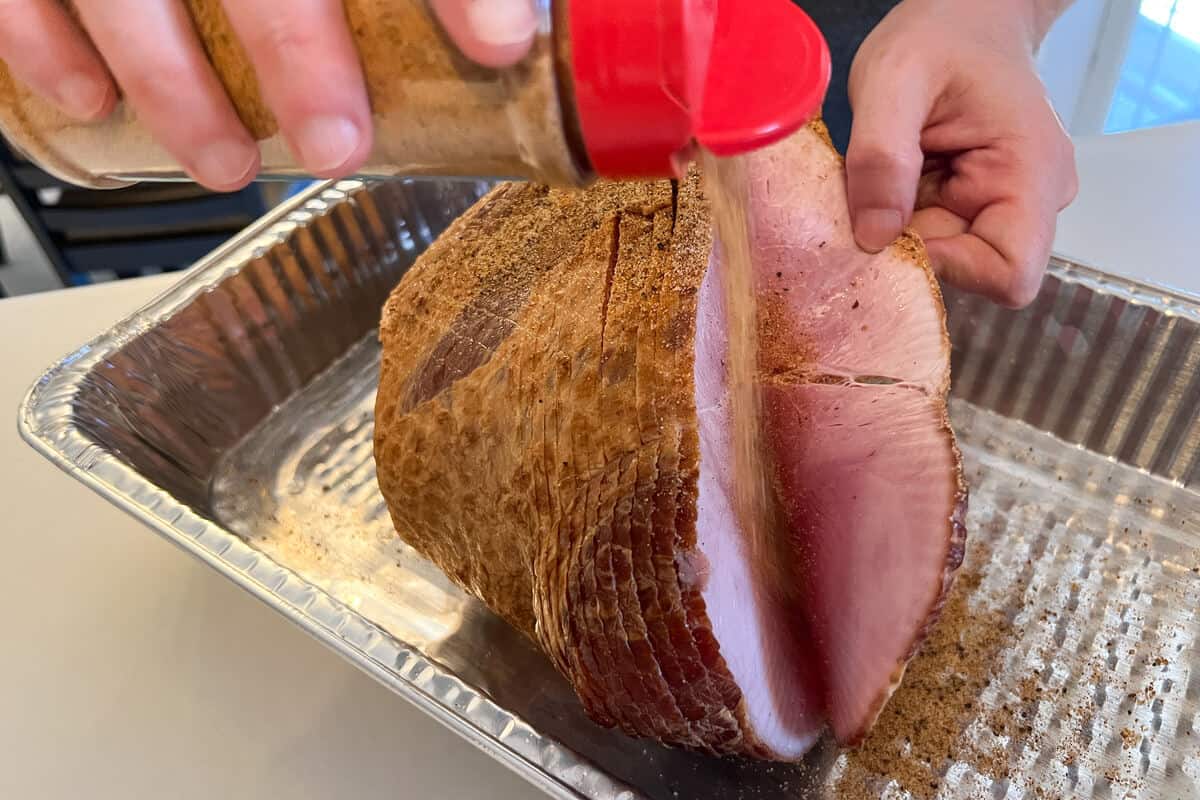 BBQ rub being sprinkled in between the spiral cut slices of ham