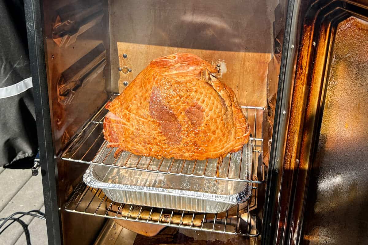 seasoned ham on the grates of a Masterbuilt electric smoker with an aluminum foil pan underneath