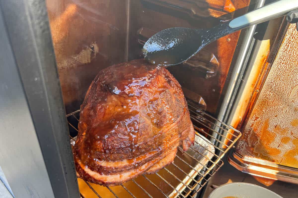 a spoon drizzling apple glaze on top of a ham in a Masterbuilt electric smoker