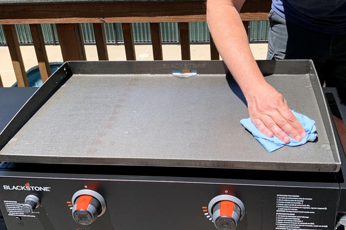 a hand wiping the surface of a Blackstone griddle with a blue shop towel