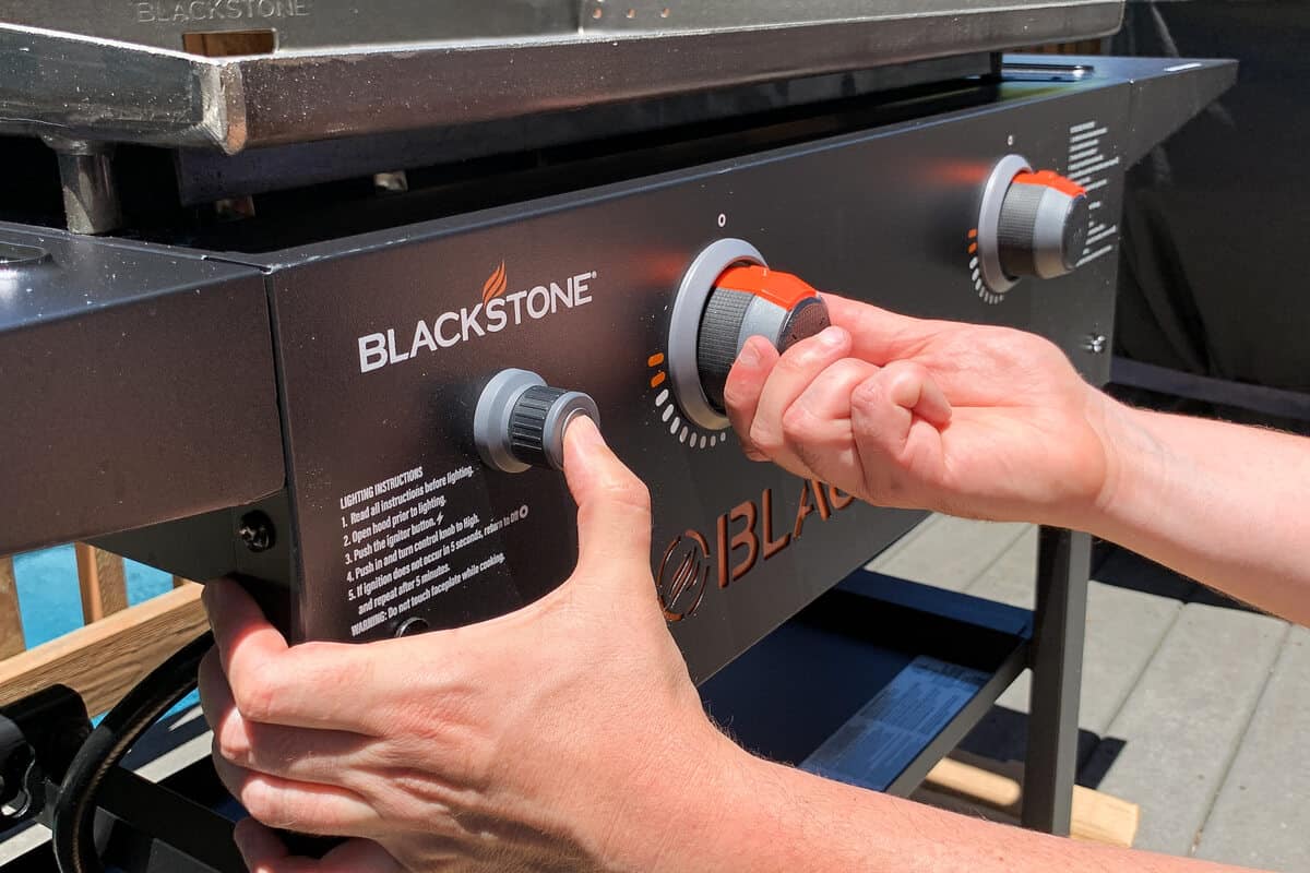 one hand turning the knob on a Blackstone griddle while the other hand presses the "ignite" button