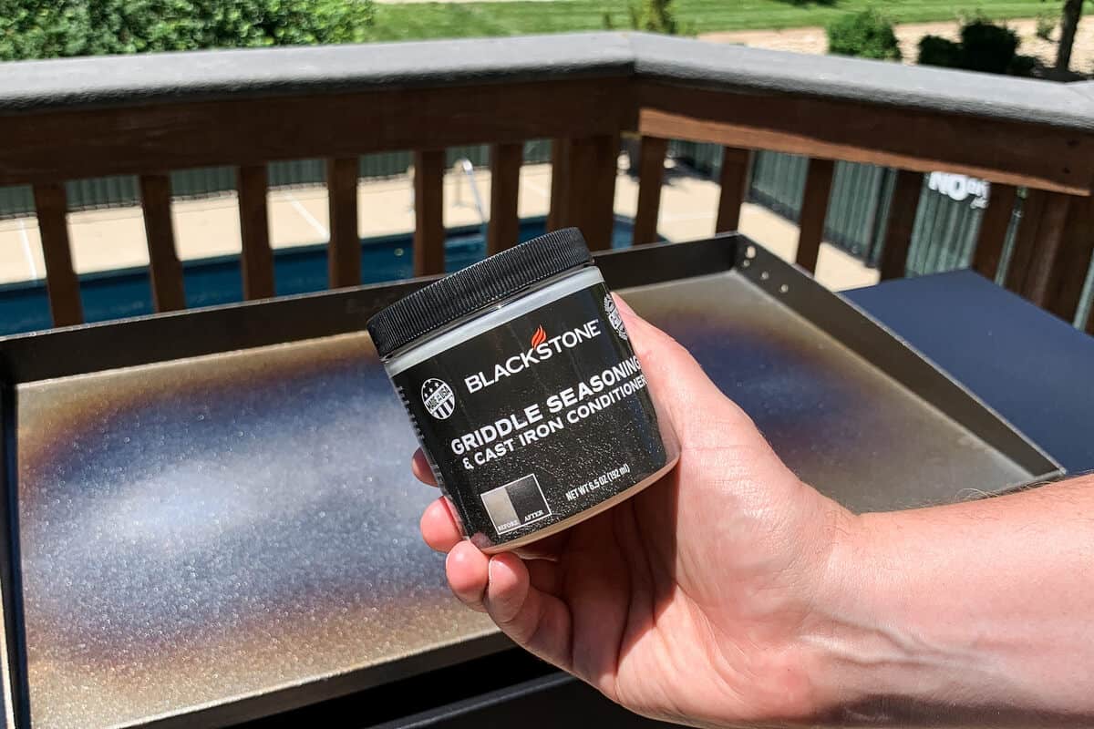 a jar of Blackstone griddle conditioner held up in front of the griddle