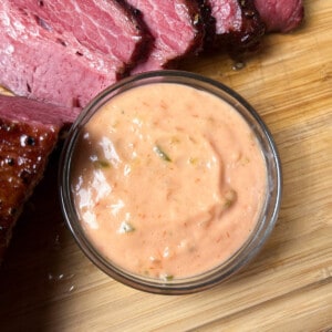 thousand island dressing in a glass bowl on top of a wooden cutting board next to slices of smoked corned beef