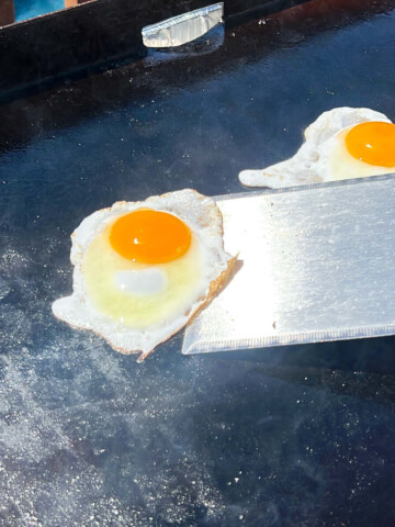 over easy eggs on a Blackstone griddle being picked up with a metal spatula