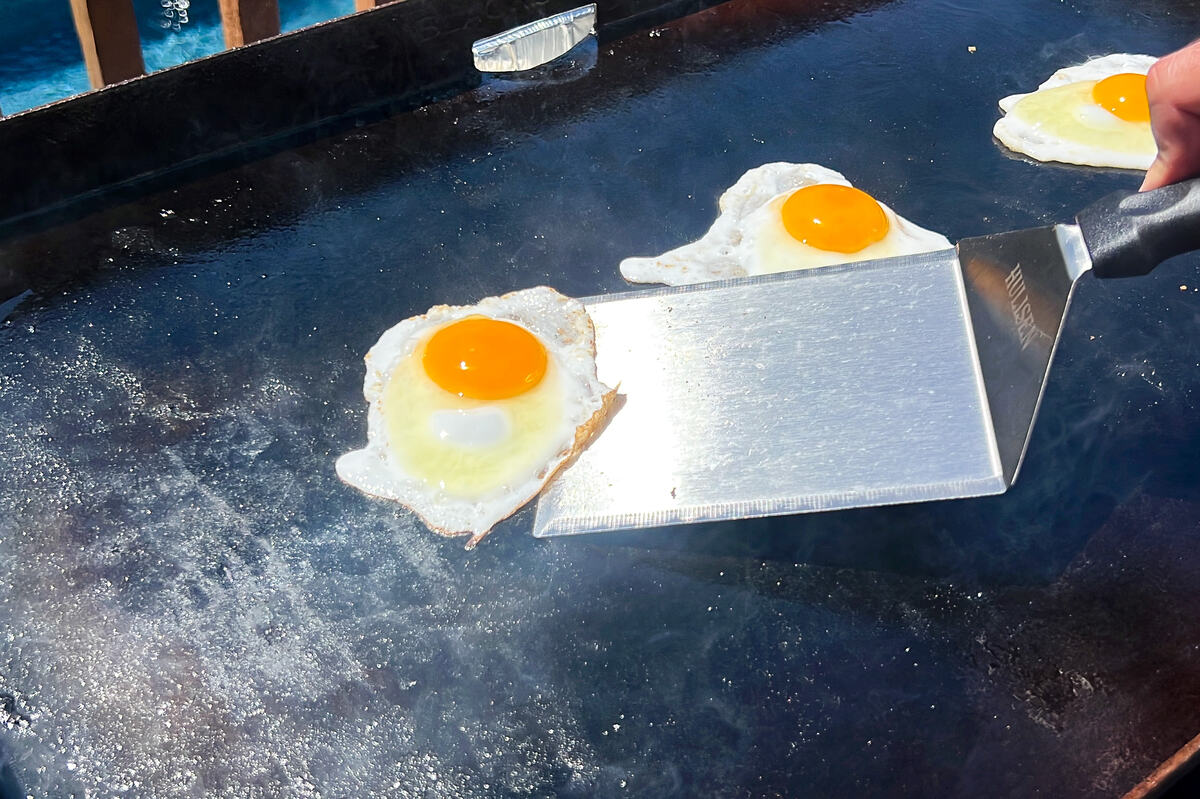 over easy eggs on a Blackstone griddle being picked up with a metal spatula