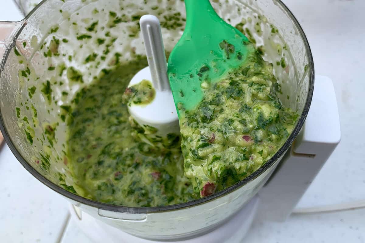 a small silicone spatula with chimichurri sauce on it above an open mini food processor