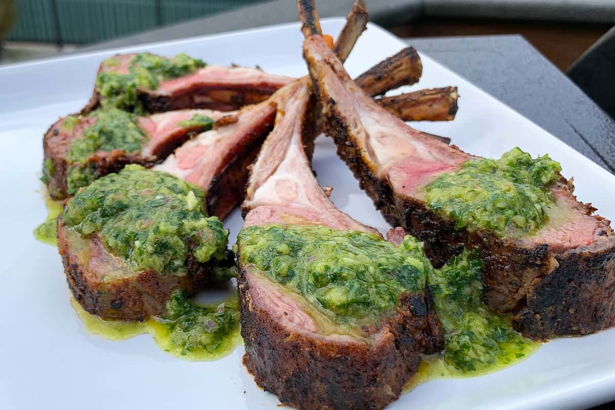 a white plate with lamb chops arranged in a circular pattern topped with chimichurri sauce