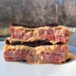 a smoked reuben sandwich cut in half and stacked on top to show the corned beef, melted swiss cheese, thousand island dressing, and sauerkraut
