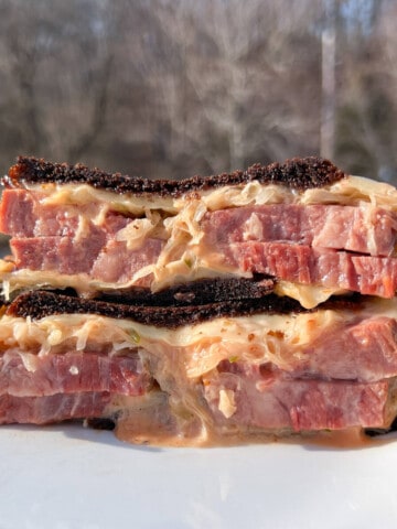 a smoked reuben sandwich cut in half and stacked on top to show the corned beef, melted swiss cheese, thousand island dressing, and sauerkraut