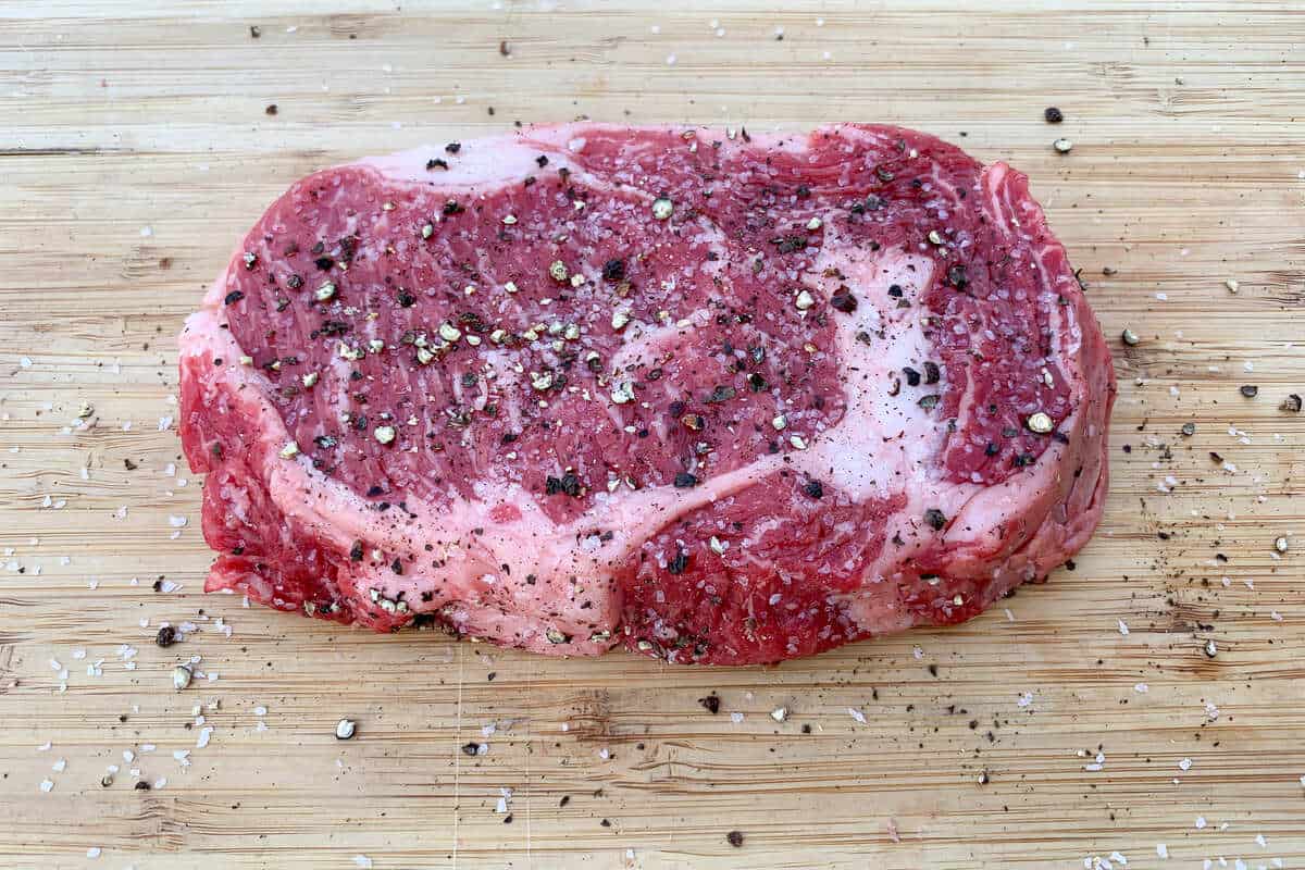 a ribeye seasoned with salt and pepper on a wood cutting board