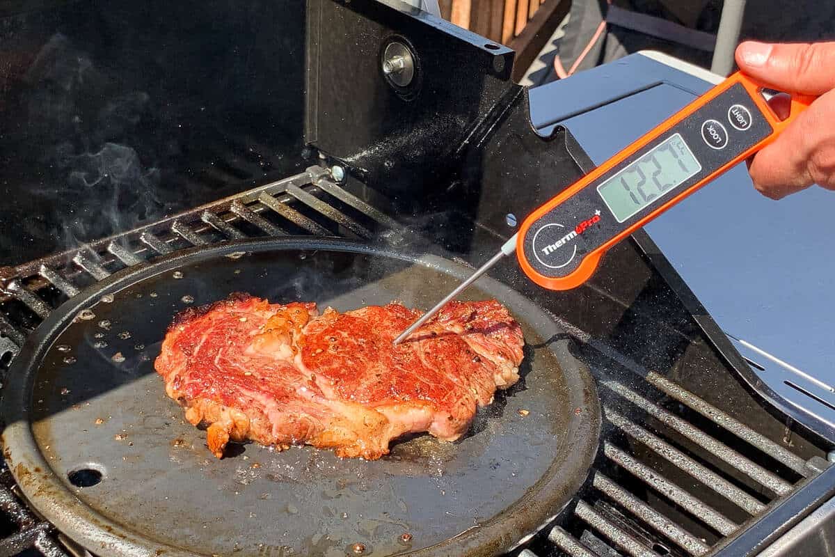 an instant read thermometer in a steak on a cast iron grill measuring an internal temperature of 122.7 degrees