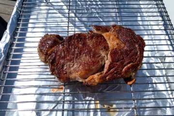 a ribeye steak resting on a wire rack over a foil lined baking sheet