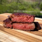 a sliced open ribeye steak on a wood cutting board to reveal a medium rare center