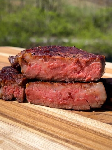 a sliced open ribeye steak on a wood cutting board to reveal a medium rare center