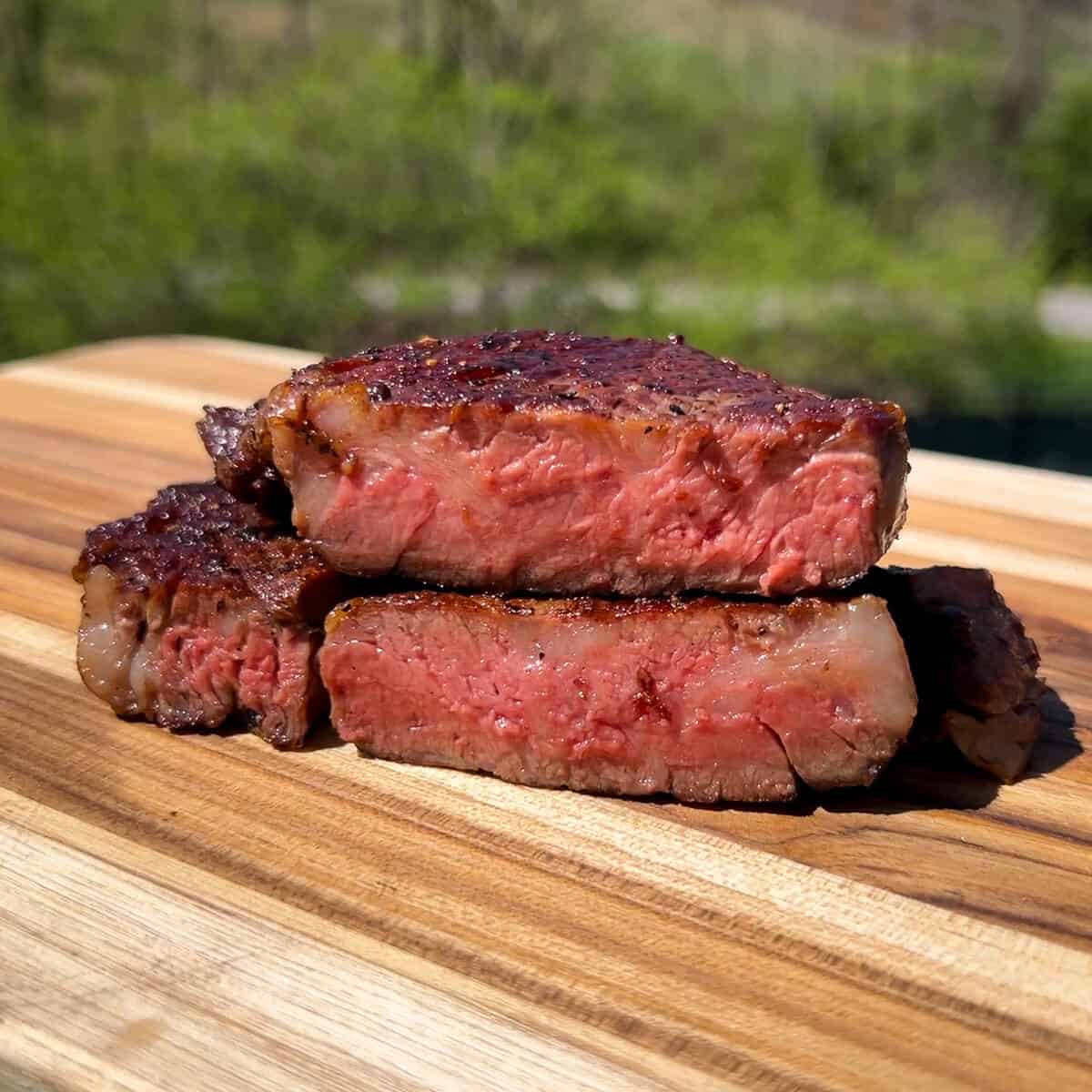 a sliced open ribeye steak on a wood cutting board to reveal a medium rare center 