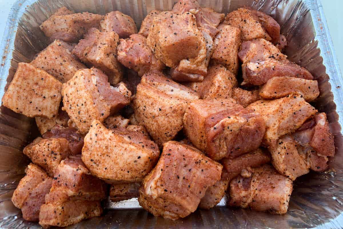 an aluminum foil pan of raw pork belly cubes seasoned with BBQ rub