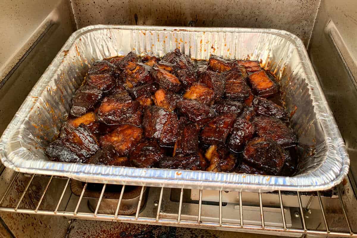 foil pan filled with pork belly burnt ends covered in BBQ sauce