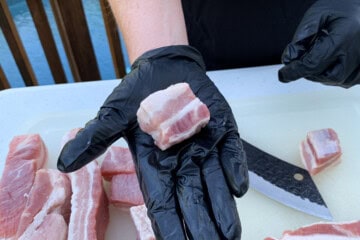 a cube of pork belly in a gloved hand