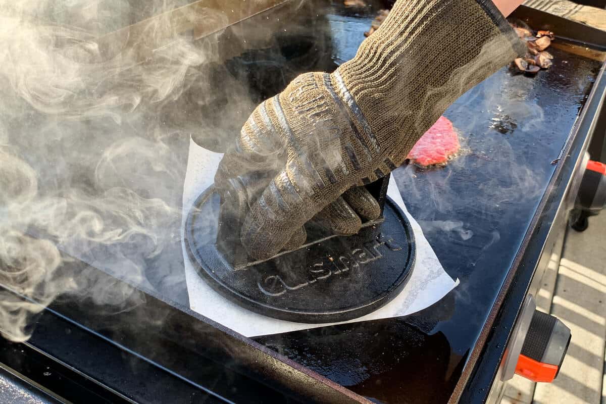 a burger being pressed on the surface of a blackstone griddle