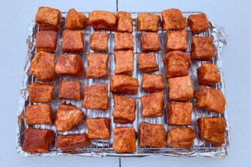 seasoned cubes of raw pork belly on a wire rack set over an aluminum foil lined baking sheet
