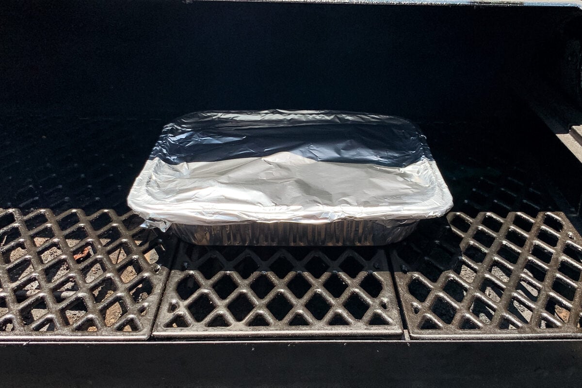 an aluminum foil pan covered in foil on the grates of a pellet grill