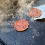 smash burgers on the surface of a blackstone griddle
