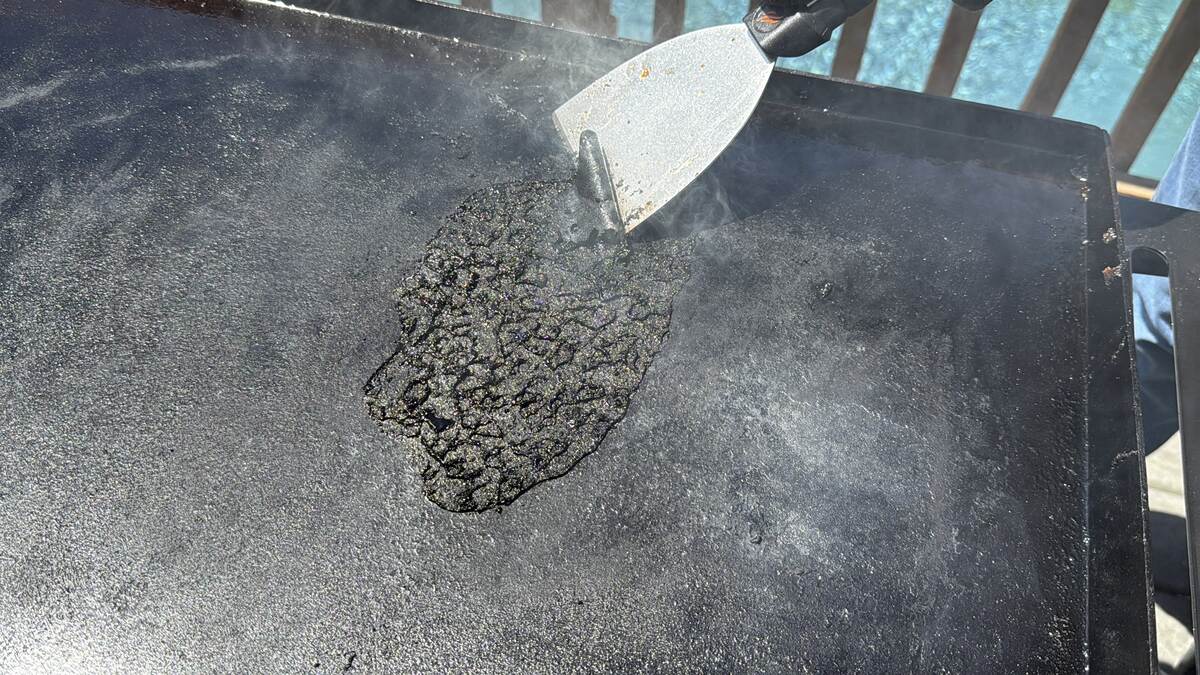 a metal scraper scraping up blackened sauce on a Blackstone griddle