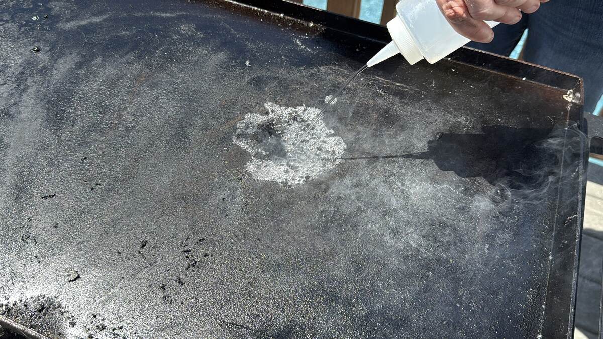 spraying water from a squeeze bottle on the surface of a Blackstone griddle