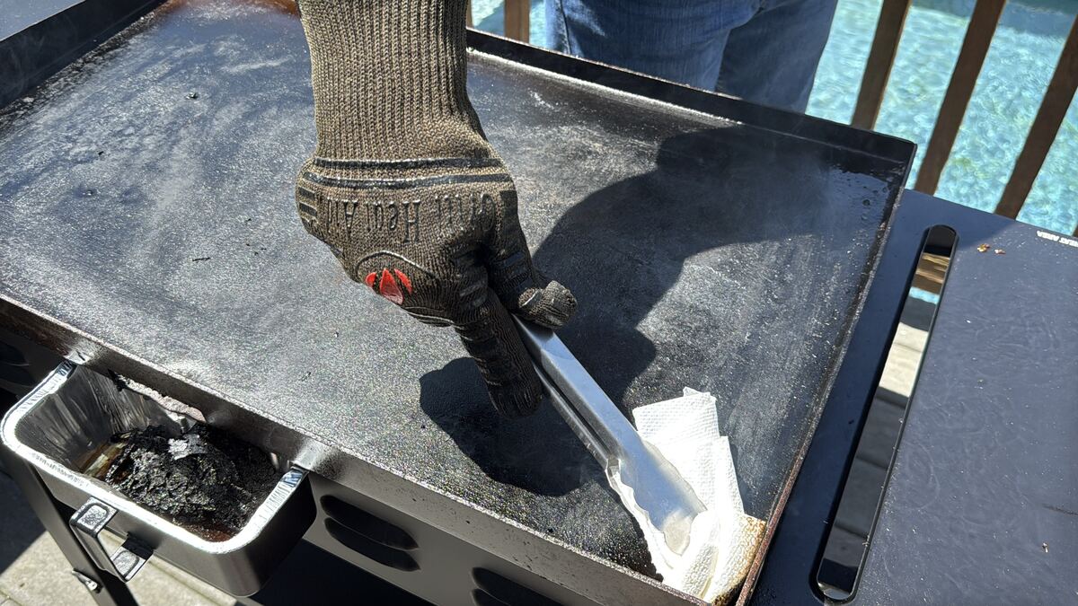 paper towels in metal tongs being pushed in the corner of a Blackstone griddle