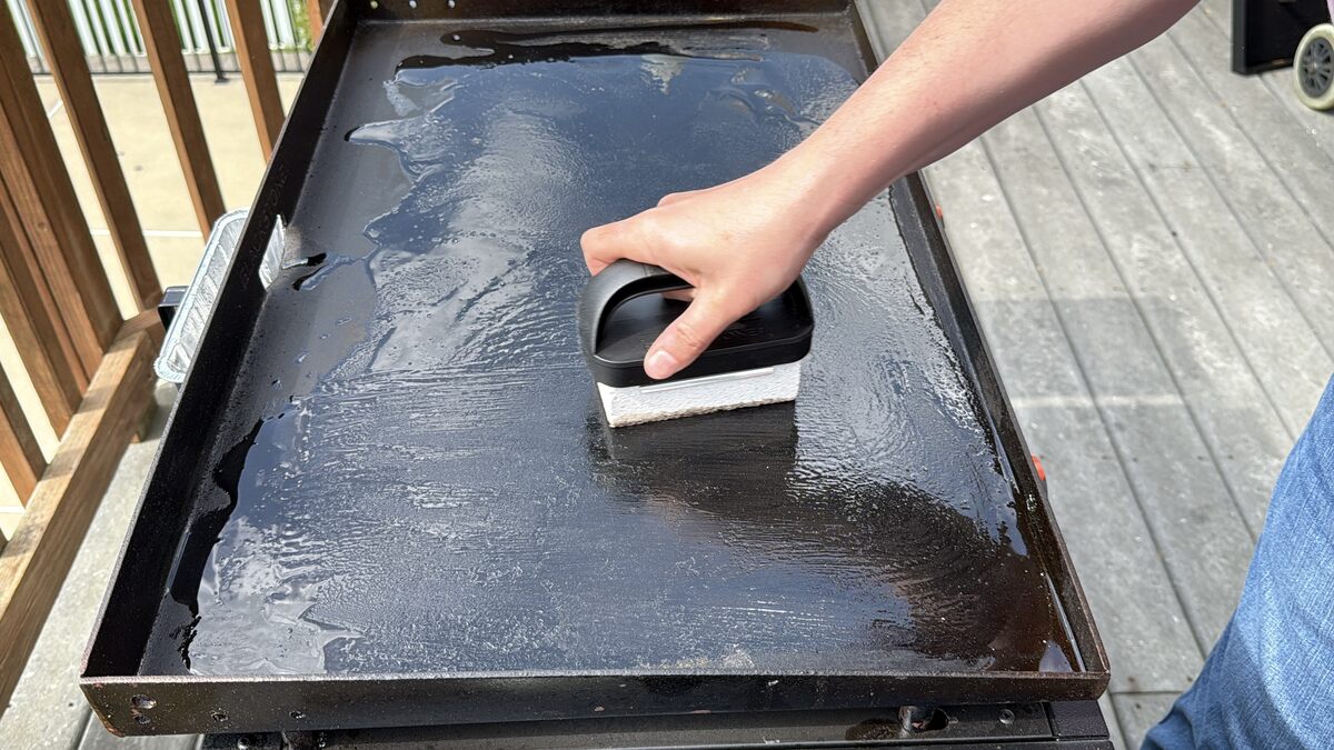 a pumice stone spreading oil on the surface of a Blackstone griddle