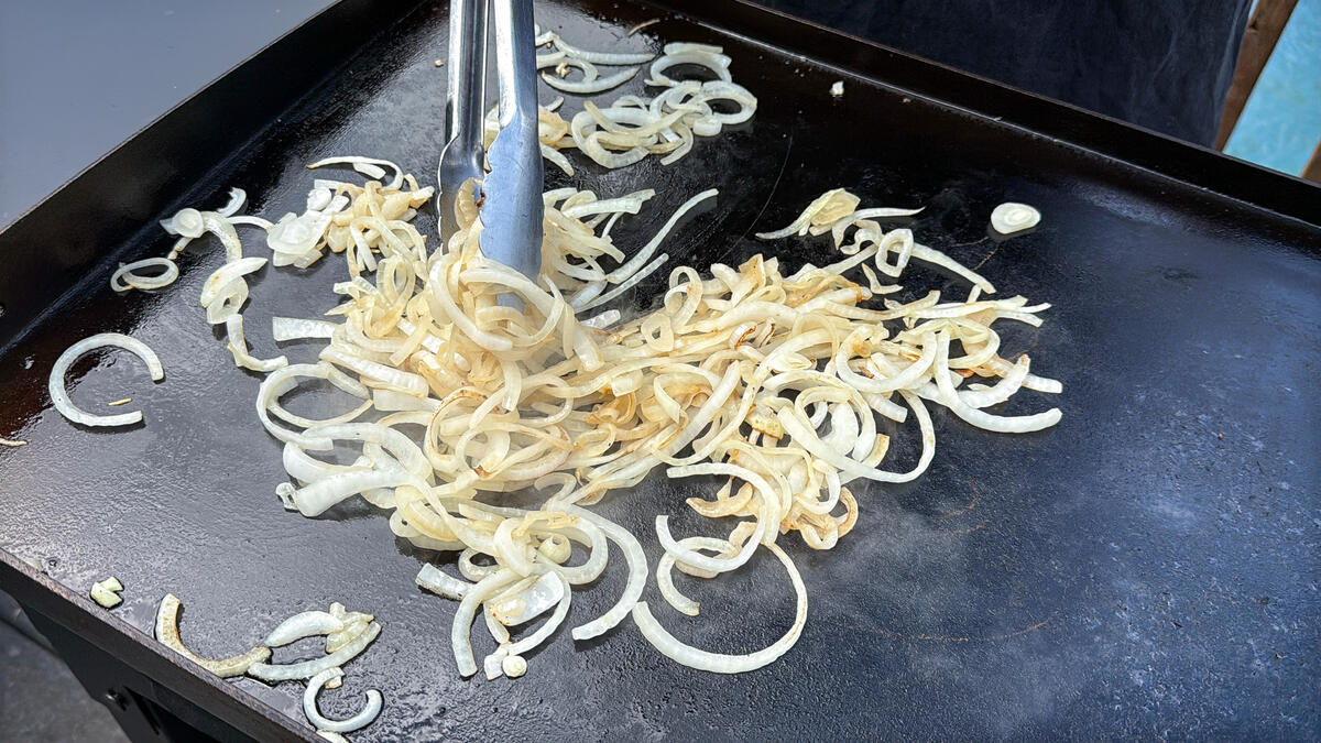 onions cooking on a Blackstone griddle being tossed with metal tongs