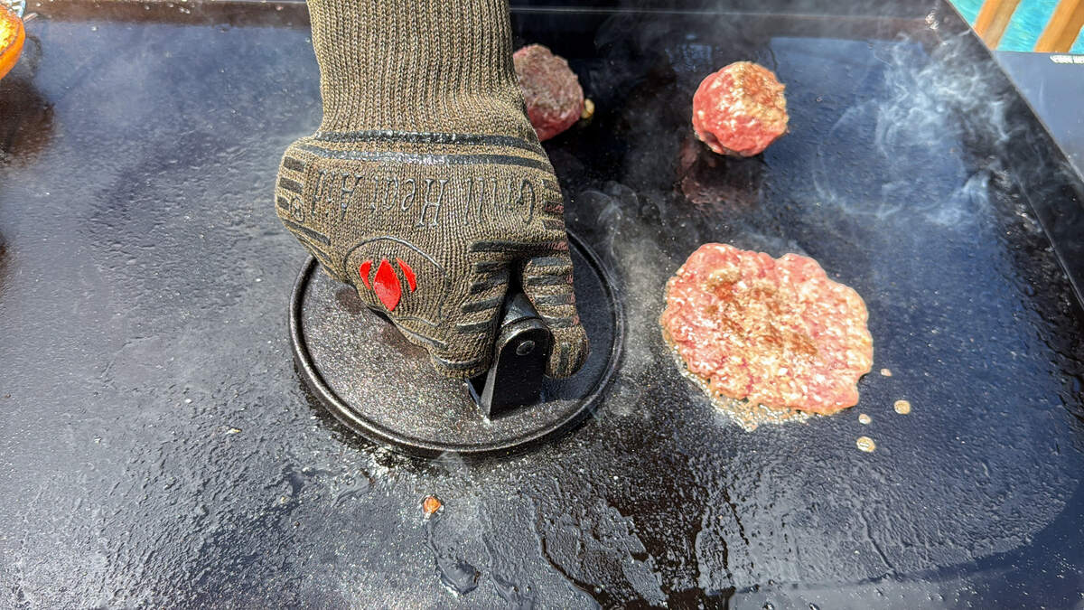 a burger press pressing down hamburger on a Blackstone griddle