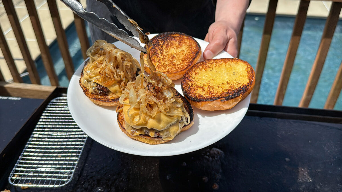 grilled onions being added to the top of smash burgers