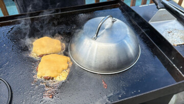 a melting dome over 2 hamburgers to melt the cheese on a Blackstone griddle
