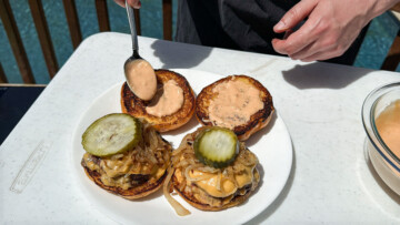 sauce being spread on the top bun of smash burgers