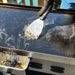 a metal scraper running across debris on a Blackstone griddle