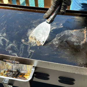 a metal scraper running across debris on a Blackstone griddle