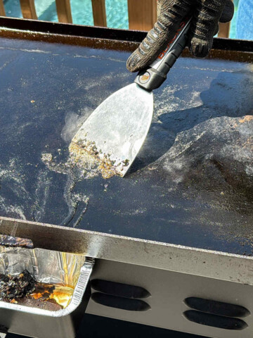 a metal scraper running across debris on a Blackstone griddle
